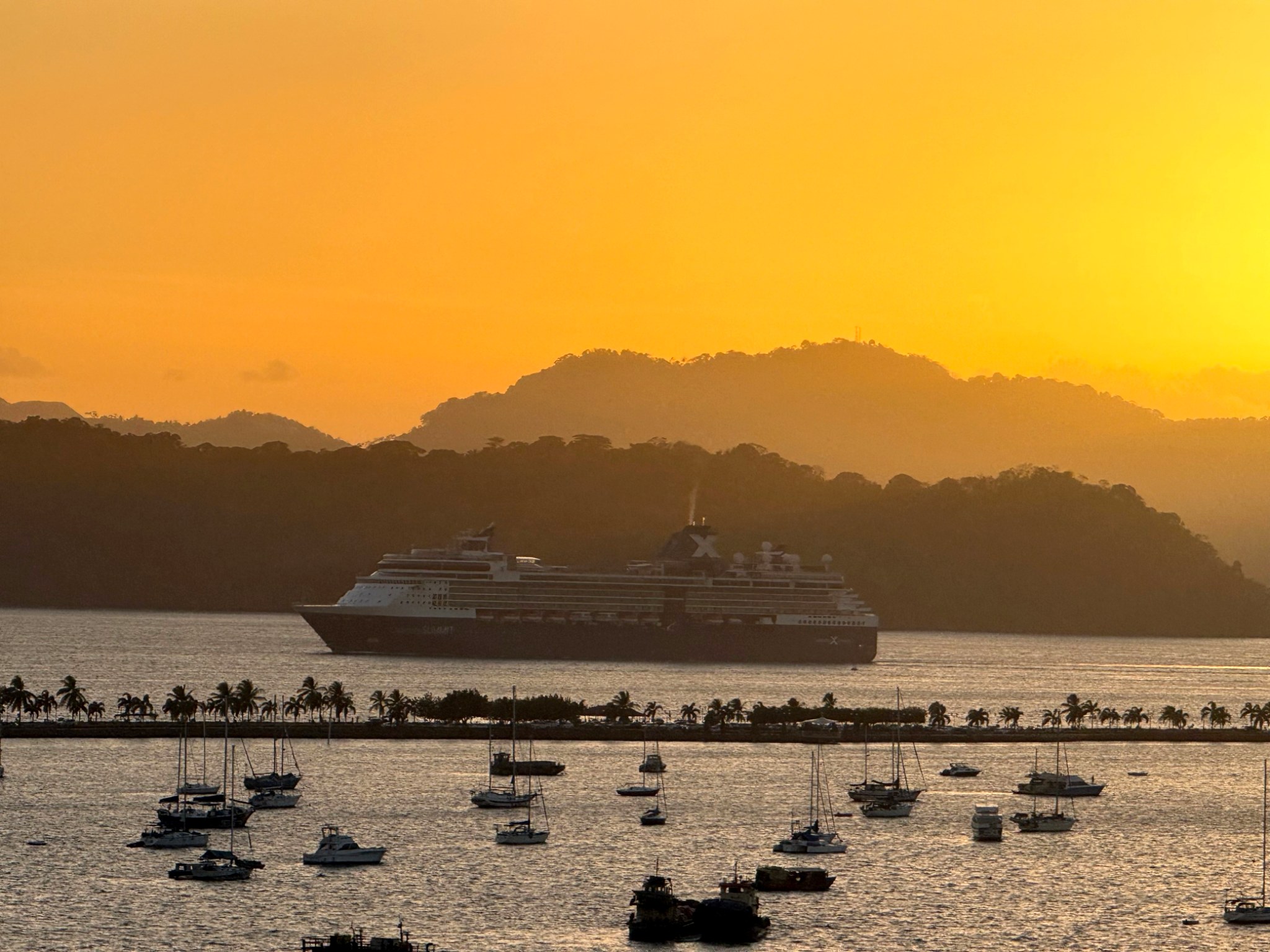 Celebrity cruise ship sailing past tropical hills at golden sunset